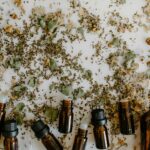 Glass bottles with essential oils surrounded by scattered dried herbs on a white surface.