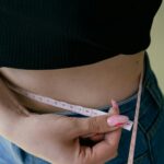 A woman measures her waist with a tape measure, focusing on fitness and weight management.